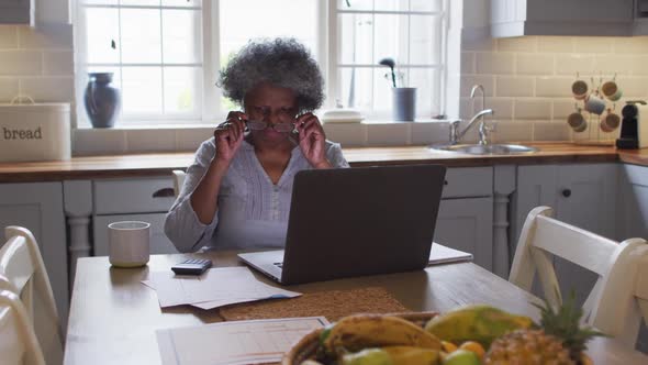 Stressed senior african american woman using laptop and calculating finances at home