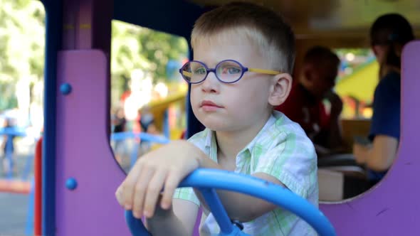 A little boy is played on the playground in a toy car. alt