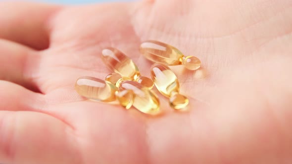 Close up of hand holding yellow transparent capsules pills organic vitamins fish oil