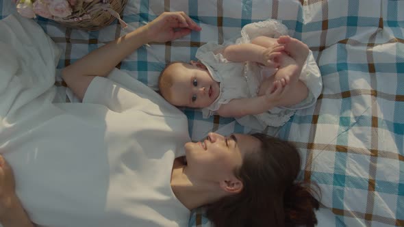 A Young Mother with a Child Lies on a Blanket