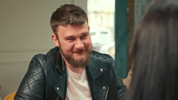 Handsome stylish hipster guy laughs in a coffee shop in the company of cheerful friends.