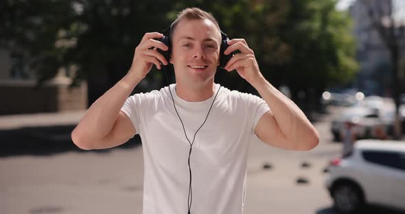 Smiling Man Puts on Big Headphones in the Summer City