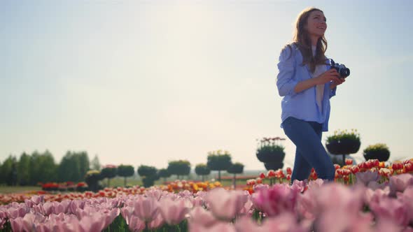 Happy Woman Touching Flowers at Walk with Camera in Tulip Field in Sunny Day