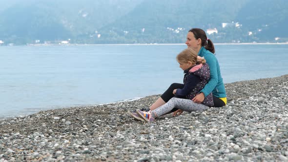 Little Girl with Mother Throwing Pebbles Into Sea