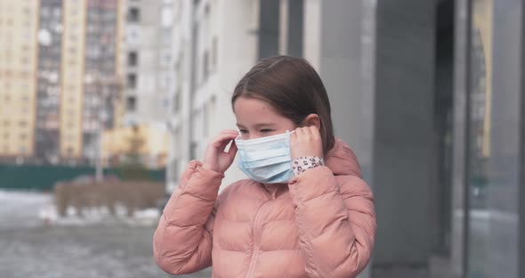 A Caucasian Girl Puts on a Medical Protective Mask Standing on a Street