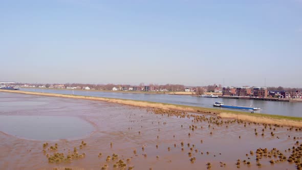 Aerial Dolly Right Across Crezeepolder Nature Reserve Rising Above River Noord With Ship Passing By