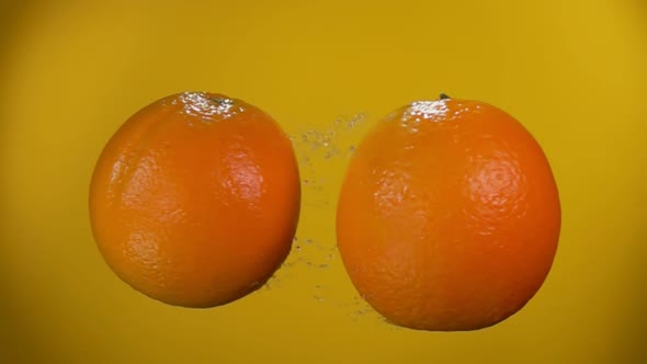 Two Juicy Oranges are Flying and Rising Drops of Water on the Yellow Background