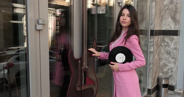 Gorgeous girl in pink near the music store with a disc