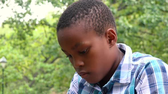 A Young  Black Boy Sits on Grass in a Park and Works on a Tablet - Closeup