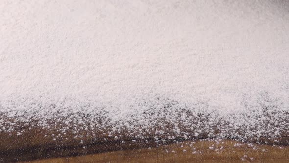 Flour is sifted through a sieve onto a wooden surface.