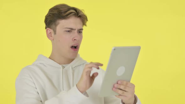 Young Man Reacting to Loss on Tablet on Yellow Background