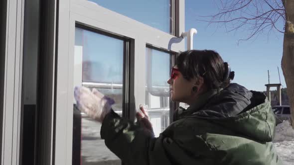 A Happy Young Woman Diligently Cleans the Glass Door