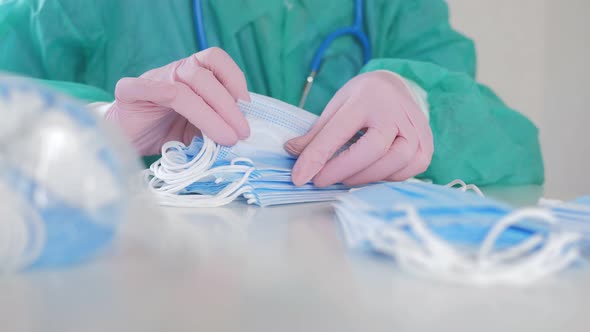 A Doctor Wearing Disposable Blue Gloves Takes a Stack of Medical Masks From a Light Table and Counts