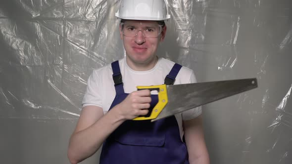 Builder in Blue Overalls and White Hard Hat Helmet and Glasses with Hand Saw