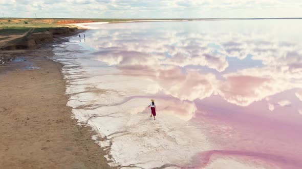 Attractive Young Woman in Red Skirt Walking Along Dry Salty Shore of Pink Lake