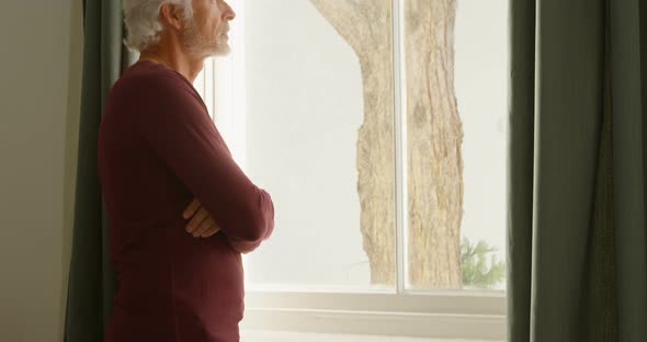 Senior man looking through window in bedroom at home 4k