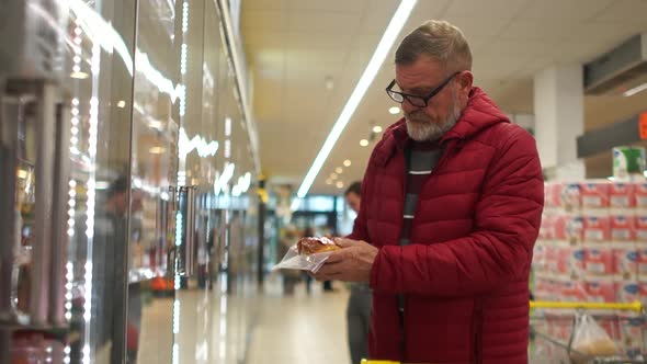 Elderly Man Pensioner with a Gray Beard and Glasses Picks Out a Meat in a Supermarket and Puts It in