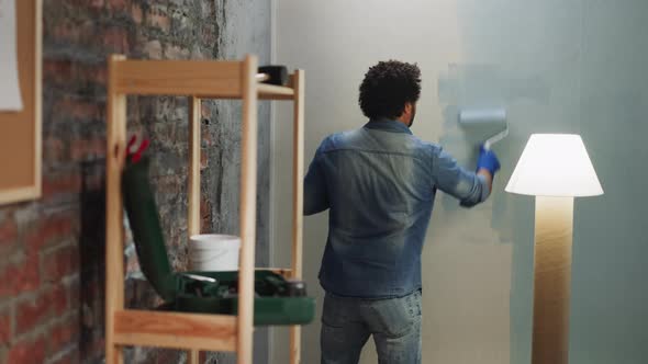 Black Man in Denim Shirt and Jeans Paints Wall in Room