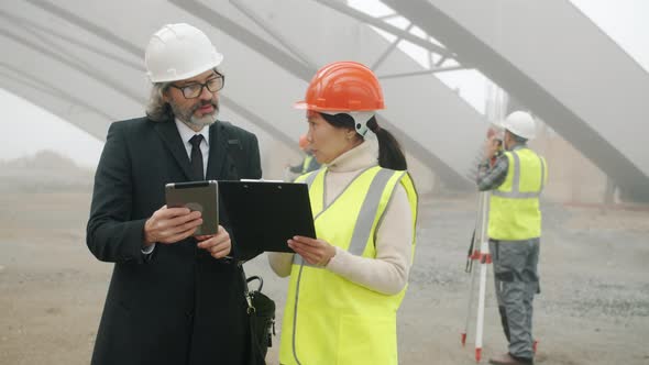 Asial Woman Engineer Talking to Caucasian Man Investor Discussing Construction Project Reading