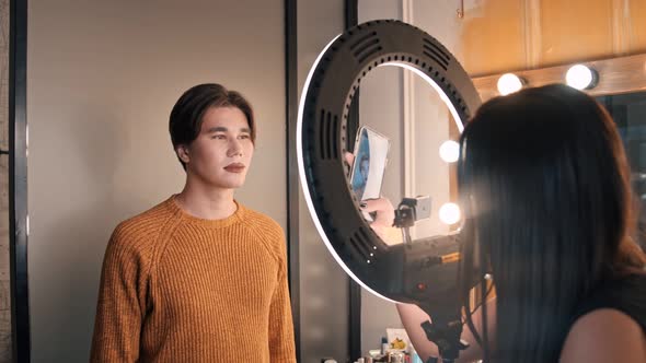 A Guy with Bold Nude Lips Sitting in Makeup Studio - the Artist Taking Photos of Him on Her Phone