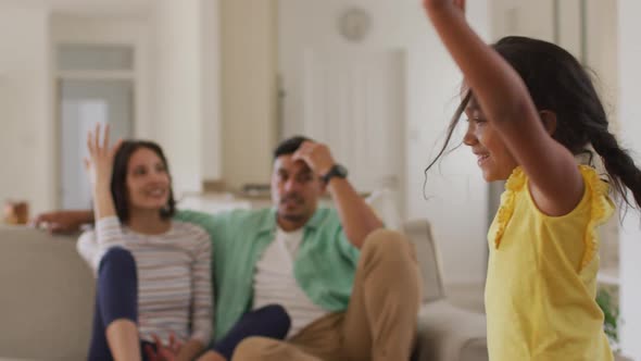 Tired hispanic parents sitting on sofa looking at dancing daughter