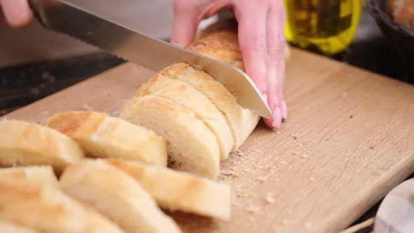 Woman Slicing Fresh Baguette Bread on Wooden Cutting Board