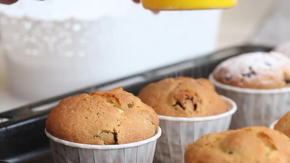 A Woman Sprinkles Icing Sugar On Freshly Baked Muffins.