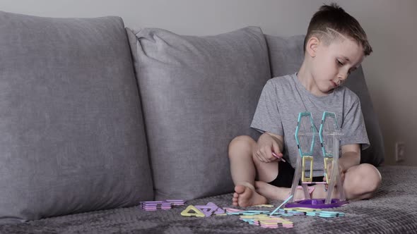 A boy in a gray T-shirt sits on a bed near a white wall and making Ferris wheel alt