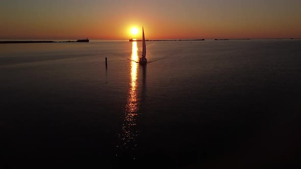 Beautiful aerial view of sailing boat on vibrant high contrast sunset over calm Baltic sea, rock pie