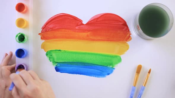 Painting Rainbow Gay Pride heart on a white paper.