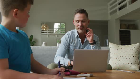 Happy caucasian father with son sitting at table and learning with laptop at home