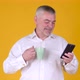 Positive adult man with a mug of coffee or tea uses smartphone texting messages in social media - VideoHive Item for Sale