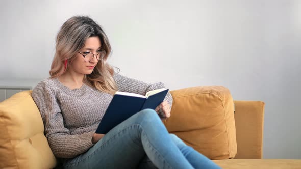 Focused Female Reading Paper Book Turning Page Smiling Relaxing on Couch