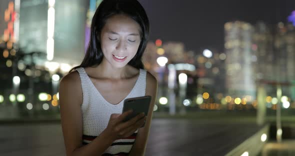 Woman looking at mobile phone in the city at night 