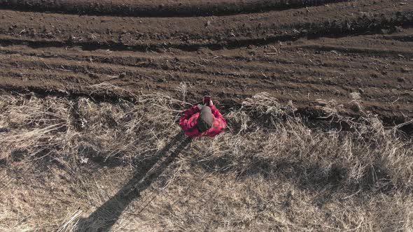 Aerial View of Woman Farmer with Digital Tablet Computer Looks at a Fresh Plowed Field After Winter