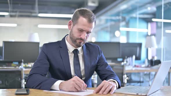 Young Businessman Writing Documents on Office Desk