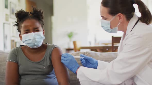 African american girl and caucasian female doctor wearing face masks, vaccinating