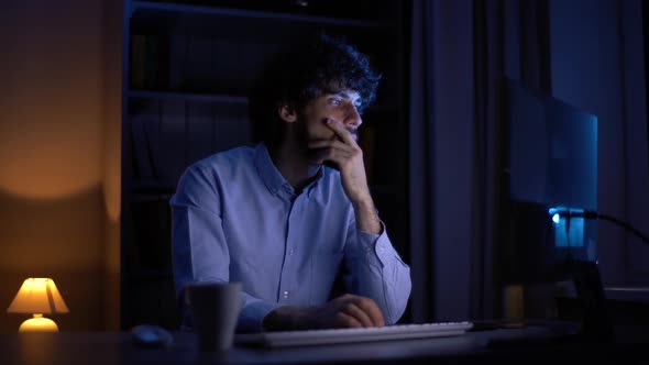 Thoughtful Young Businessman Working on Computer at Late Night at Home Office