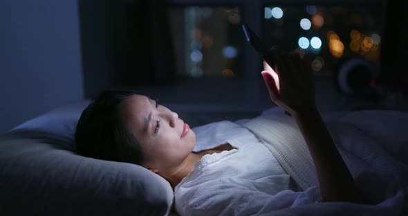 Woman use of mobile phone on bed at night