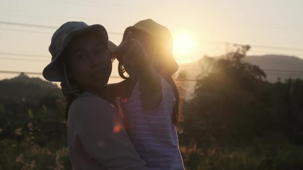 Silhouette of cute daughter hugging and kissing her loving mother at sunset at summer garden.