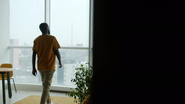 Young Man in Casual Clothing Walking to Window in Kitchen at Home Watching Beautiful View Alone