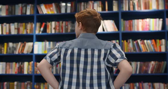 Back View of Teen Boy Choosing Book on Bookshelf in Library