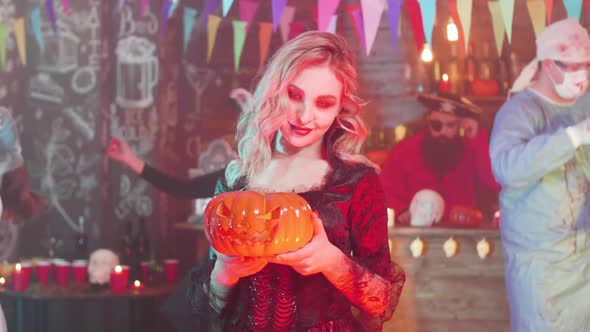 Sexy Vampiress with a Jack-o-lantern in Her Hands at a Halloween Party