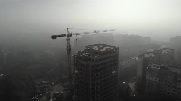 Birds eye view on tower crane in fog standing next to residential building.