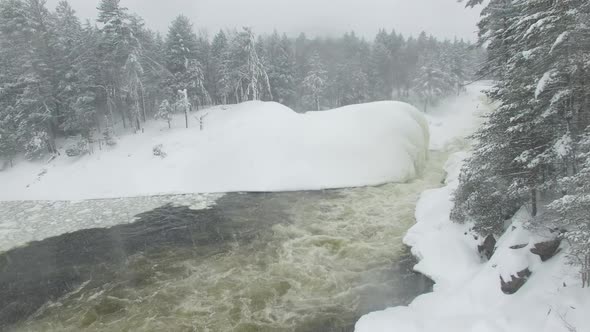 Slow rising drone filming forest's edge with snow covered pine trees and river