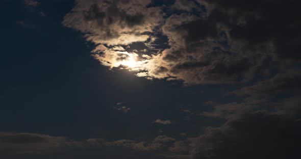 Timelapse of full moon hiding behind clouds. Clouds passing by warm moonlight