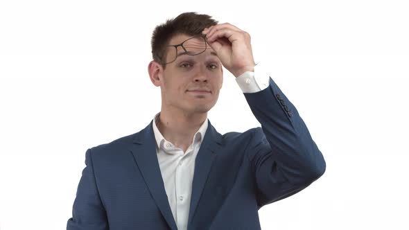 Handsome Businessman in Blue Suit Takingoff Glasses and Wiping Lenses Standing Over White Background