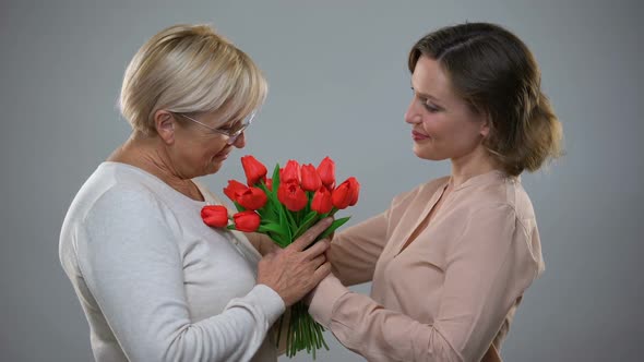 Young Female Presenting Senior Mother With Tulips and Hugging, Love and Care