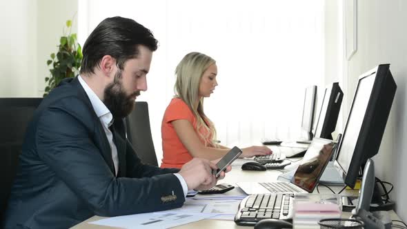 Man Works on Smartphone and Woman Works on Desktop Computer in the Office (Workers)