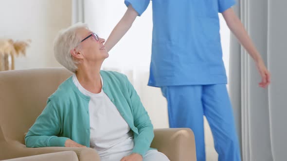 Positive nurse in blue uniform comes to hug lonely senior woman